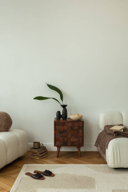 istock A cozy living room interior featuring two white sofas, a wooden side table with decorative items, a soft rug, and books stacked on the floor. The minimalist design creates a warm and inviting atmosphere. 2178686549