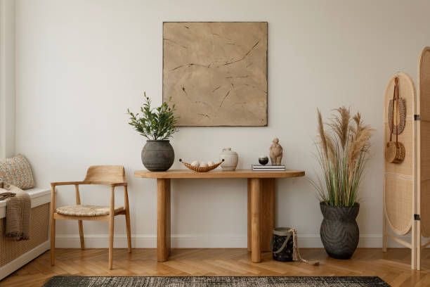 istock Modern living room interior with a minimalist design. Features a wooden table adorned with decorative vases and sculptures, a wooden chair with a woven seat, and a large abstract painting on the wall. Natural light highlights the calm and cozy atmosphere. 2178689841