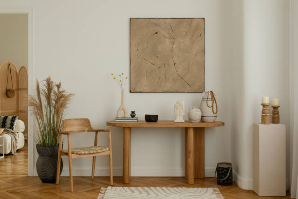 istock Modern living room interior with a minimalist design. Features a wooden table adorned with decorative vases and sculptures, a wooden chair with a woven seat, and a large abstract painting on the wall. Natural light highlights the calm and cozy atmosphere. 2178689932