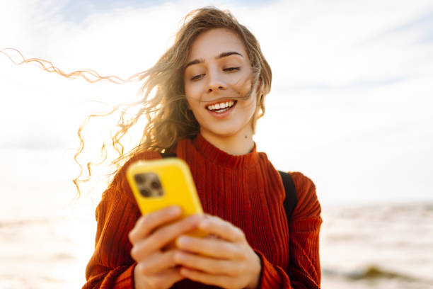 istock Young woman using mobile phone at beach. Cold weather. Autumn. 2178690785