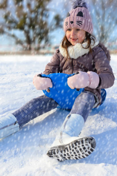 istock Young girl enjoying a snowy day while sledding down a hill wearing winter attire 2178691678