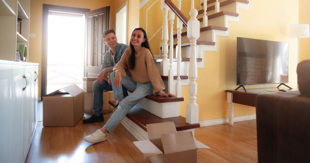 istock A happy couple sits on the staircase in their new home, taking a break from unpacking boxes. The warm, inviting interior and their relaxed smiles capture the joy and satisfaction of being together. 2178693885