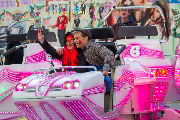 A young man and a woman take a selfie in a pink cart on a carousel A young man dressed in a checked shirt and a brown hat and a woman with a red wig and painted face take a selfie in a pink cart on a carousel during the carnival parade in Cologne. mardi gras body painting stock pictures, royalty-free photos & images