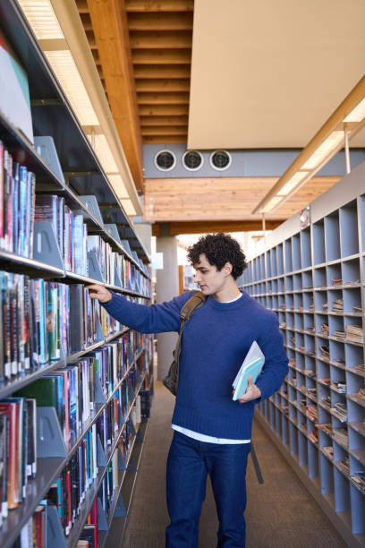 istock Young male student searching for book in college library 2178702856