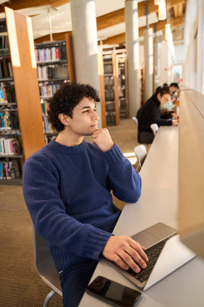 istock Thoughtful student working on laptop in busy college library 2178702973