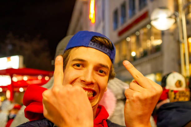 A smiling young man with a blue cap on his hood backwards raises his fingers during the Rosenmontag carnival parade in Cologne.