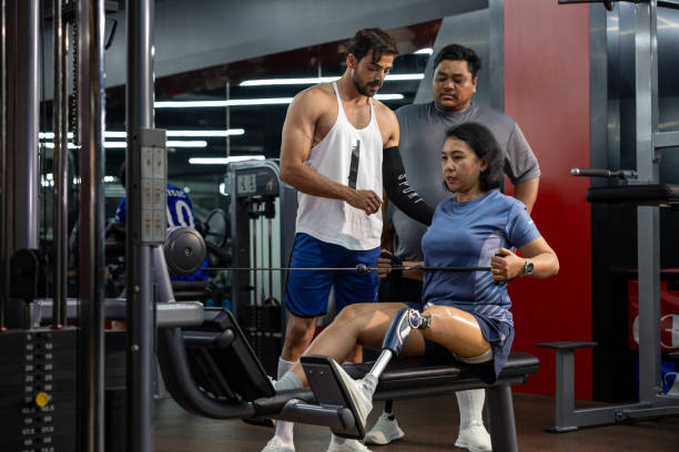 istock Asian woman with prosthetic leg from amputation from doing weight training workout exercise using machine at gym with professional trainer for handicap and disability people and recovery 2178706804