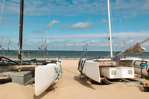 The Hague, Netherlands - July 11, 2024: Catamaran boats on the beach in Scheveningen, district of The Hague. North Sea with ships in the background, blue sky with clouds.