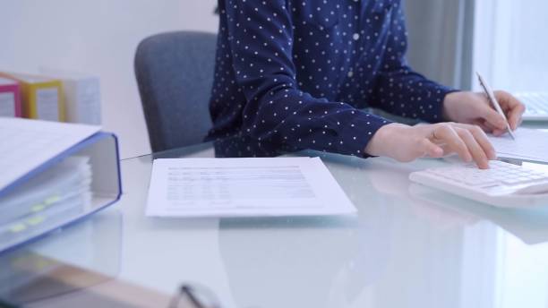istock A female accountant with blue dotted blousy is using a laptop computer and calculator to calculate taxes at a glass desk in the office. Right side view 2178714359