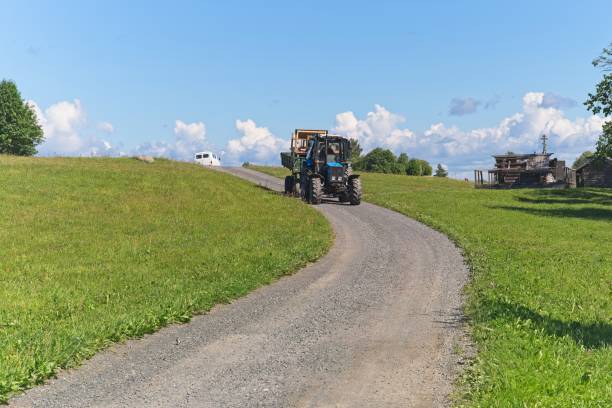 Kizhi Island, Russia, July 10, 2024. Vintage tractor driving along road in museum-reserve, mown green fields, wooden buildings, sky and clouds, rural landscape, agricultural machinery, sunny day, summer.