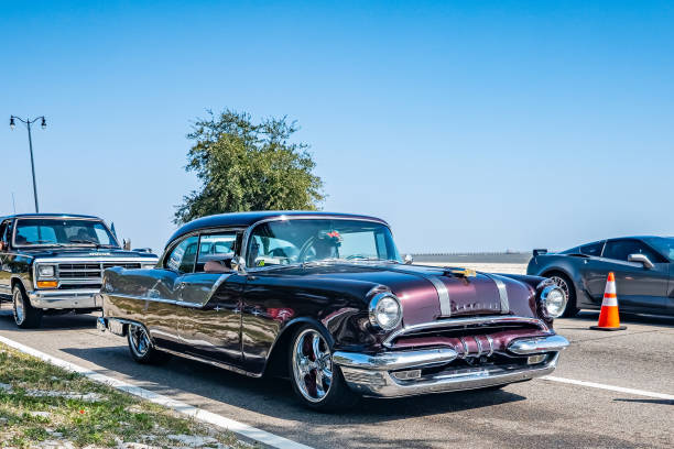 A detailed close-up of a vintage car's rear light and shiny chrome bumper. The sleek lines and polished finish of the car reflect its classic design and well-maintained condition, with a hint of green grass in the background.