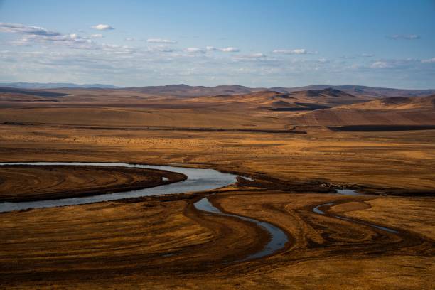 A drone view of a winding river flowing through a vast, arid landscape under a blue sky in Nei Mongol, China