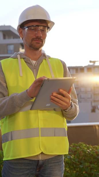 istock Male engineer with white helmet and safety vest is taking notes on a digital tablet while inspecting a construction site at sunrise in early morning, vertical front view. Architecture and engineering 2178741719