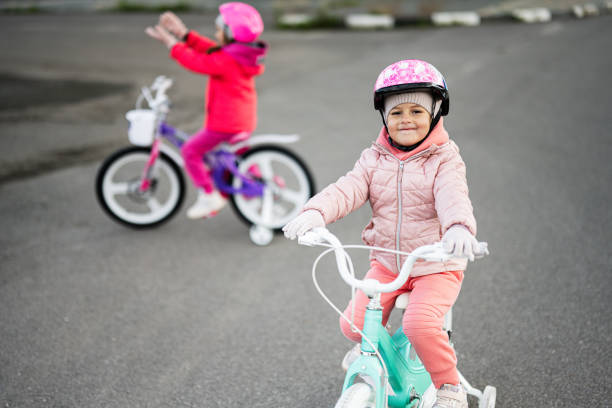 Two young children, dressed in warm clothing and helmets, happily ride their bicycles on an empty road during a winter day, showcasing joy and outdoor activity.