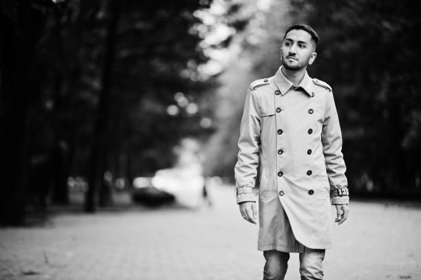 Stylish kuwaiti man at trench coat walking at park.