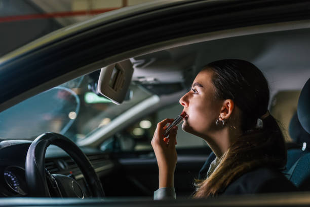 istock Young woman putting a red lipstick while sitting in a car. 2178748105