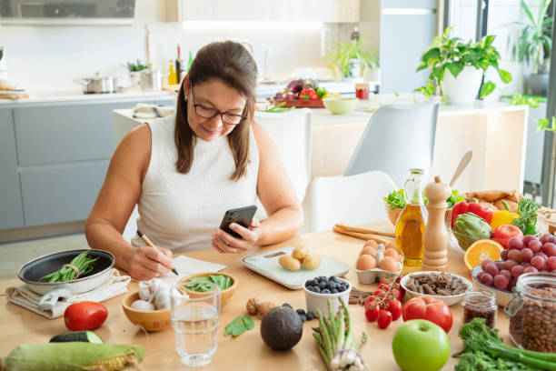 istock Woman in kitchen taking notes, researching recipes with cell phone for well balanced diet 2178751960