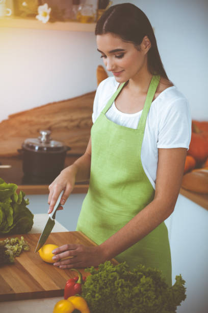 istock An attractive young dark-haired woman preparing delicious fresh vegetarian salad while standing and smiling in sunny kitchen. Cooking and householding concepts 2178763535