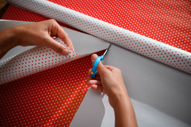 istock Person wrapping a gift with red and white polka dot wrapping paper using scissors 2178764981