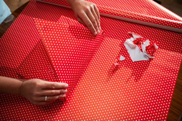 istock Hands wrapping a present with red polka dot paper on a wooden table signify creativity and preparation for a special occasion or a festive celebration, highlighting a personal and thoughtful touch. 2178765018