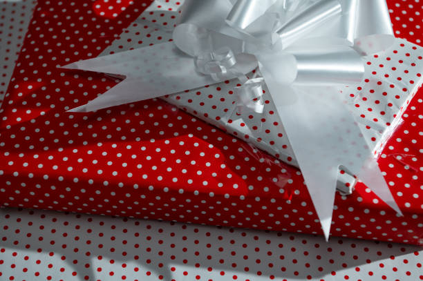A beautifully wrapped gift box with a white ribbon sits on a vibrant red polka dot background, exuding a festive and celebratory vibe.