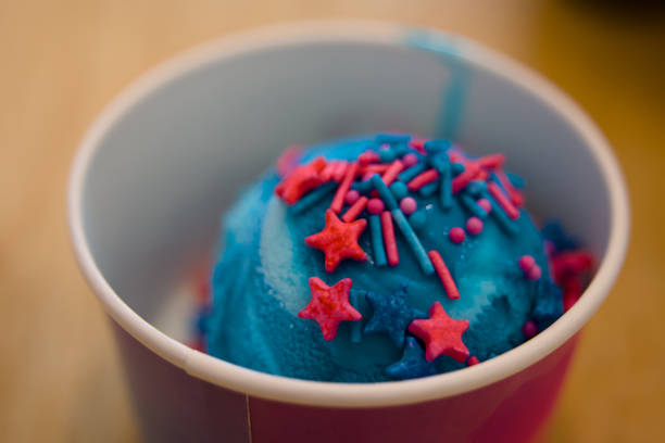 A scoop of vibrant blue ice cream topped with colorful sprinkles and sugary stars in a festive paper cup.