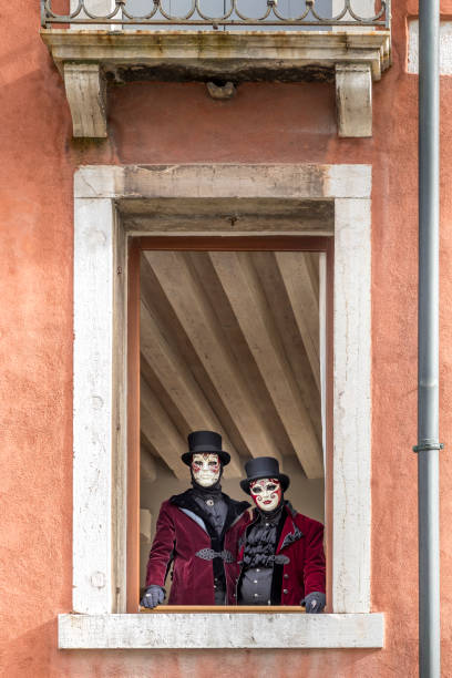 Venice, Italy - February 11, 2024: 2 masked people looking through window during carnival in Venice, Italy