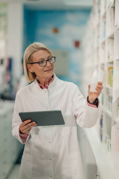 istock Senior female pharmacist holding medicine bottle and using digital tablet in a pharmacy 2178779117