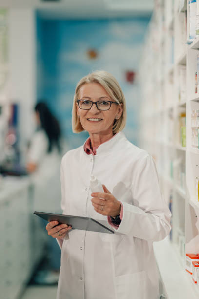 istock Senior female pharmacist holding medicine and using digital tablet in pharmacy 2178779129