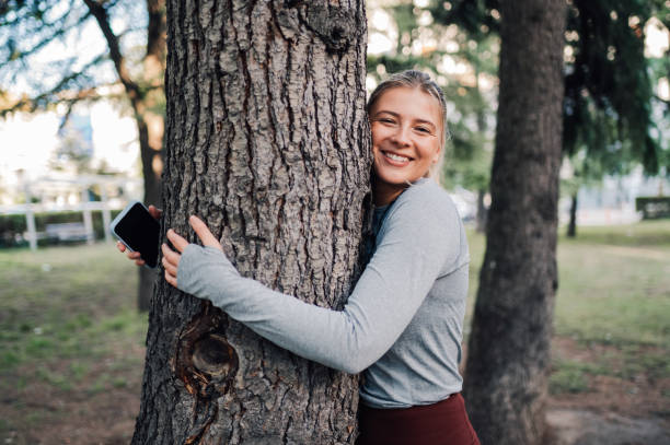 Young sportswoman hugging a tree in the park while holding her smartphone