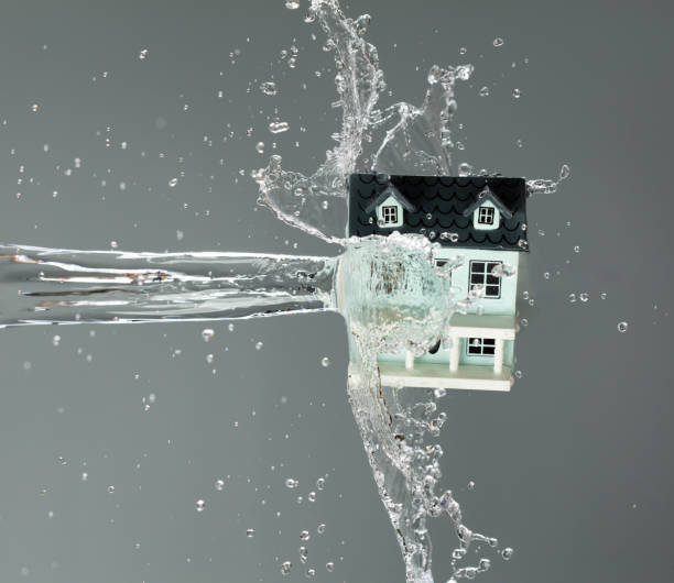 Mini House home sits on climate change while Heavy Flood flow to house and hit wall as protection insurance over gray background to show happy smile mini house home on flood water