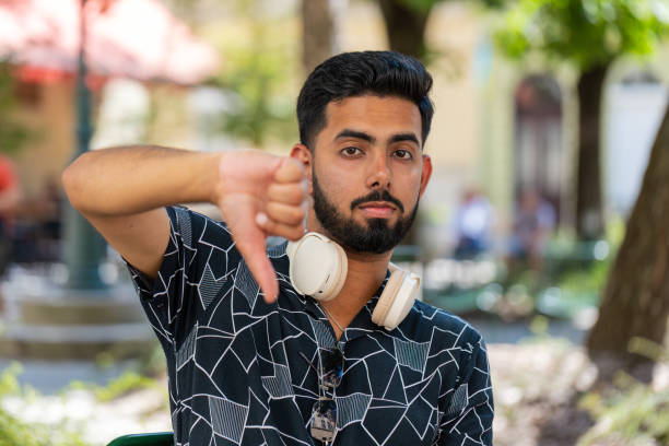 Dislike. Portrait of young man male showing thumbs down sign gesture, expressing discontent, disapproval, dissatisfied bad work, mistake. Displeased stylish tourist sitting on city street outdoors.