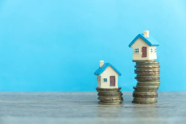 istock Coins ascending stack with miniature house on top over a blue wall. 2178793656
