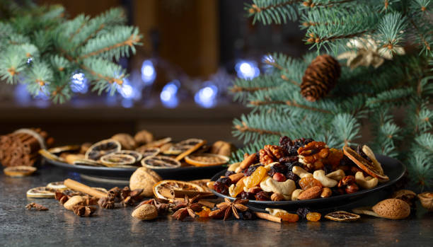 Christmas spices, various nuts, raisins, and dry citrus slices on a kitchen table. Christmas still-life with spruce branches and dried fruits.