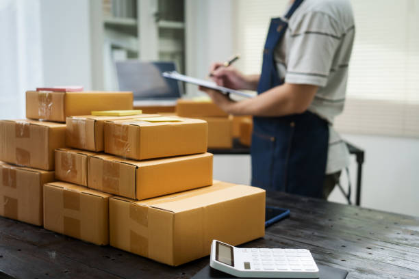 A man is working at his desk, preparing parcel boxes for shipment. He checks and packs items carefully, using shockproof materials, and attaches labels before sending them to customers via EMS.