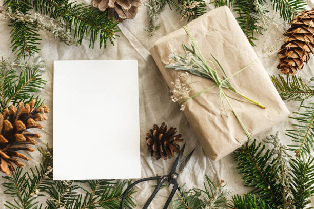 istock Christmas card mock up. Empty greeting card and stylish zero waste gift on rustic table with fir branches and pine cones flat lay. Space for text. Season's greetings postcard template. Eco friendly 2178807981