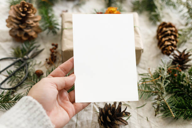 istock Christmas card mock up. Hand holding empty greeting card on rustic table with fir branches and pine cones. Space for text. Season's greetings. Zero waste postcard template. Merry Christmas 2178808059