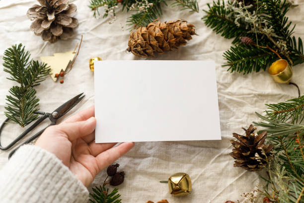 istock Christmas card mock up. Hand holding empty greeting card on rustic table with fir branches and pine cones. Space for text. Season's greetings. Zero waste postcard template. Merry Christmas 2178808110