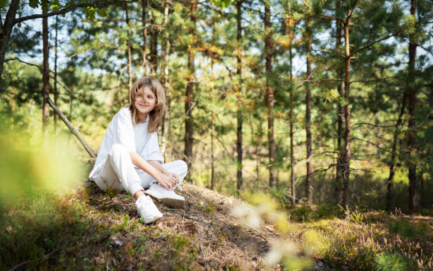 istock Young girl enjoying a sunny day in a forest clearing while sitting on a grassy mound surrounded by trees and nature 2178810927