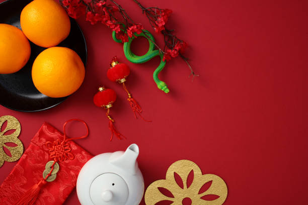 istock Chinese New Year flat lay with traditional decorations: oranges on a black plate, red envelopes, snake, gold cutout flowers, red lanterns, and a teapot on a red background. Happy Lunar New Year 2025 2178815308