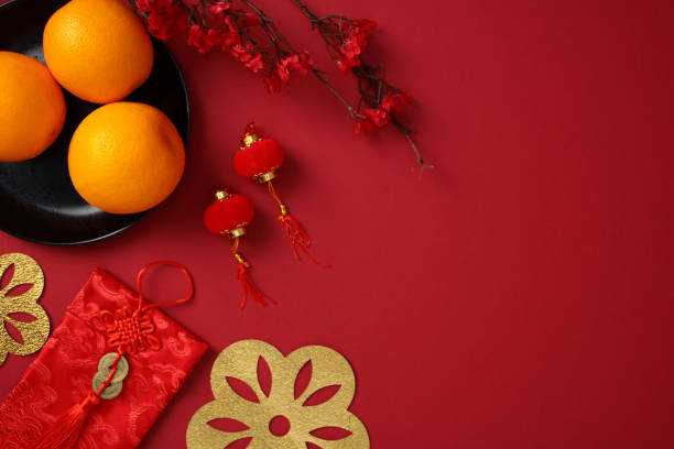 istock Chinese New Year still life with oranges on a black plate, envelope with red tassel decorations, lanterns, and golden cut out flowers on a red background. Lunar New Year greeting card design 2178815355