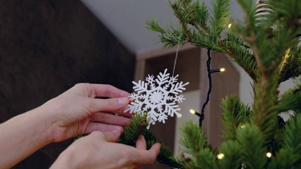 istock Woman decorating christmas tree with lights and snowflake ornament, getting ready for christmas and new year celebration. New Year's Eve with family 2178815453