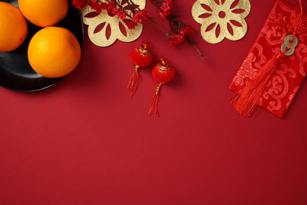 istock Lunar New Year flat lay composition with traditional Chinese decorations: oranges on a black plate, red envelopes, gold cutouts, and red lanterns on a vibrant red background 2178815484