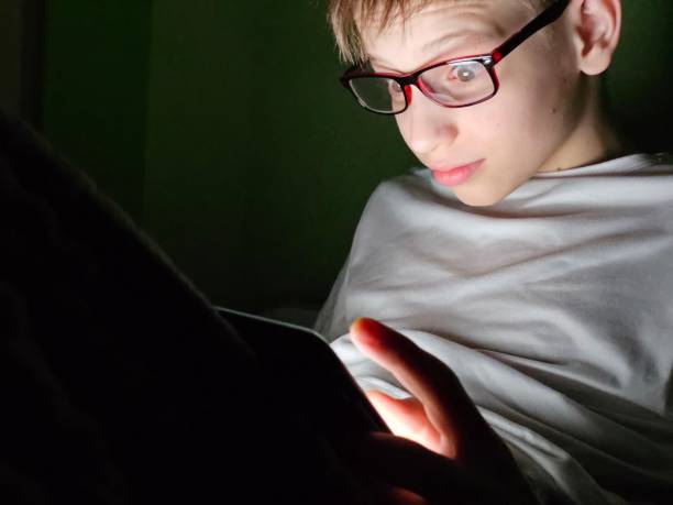 istock A boy with glasses intensely focused on a mobile device in a dimly lit room during nighttime concept 2178818694
