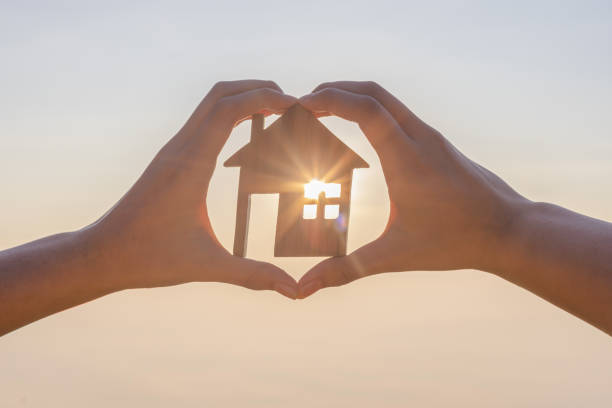 istock Woman's hand holding model house on morning sunrise sky with sun rays solar power. 2178819364