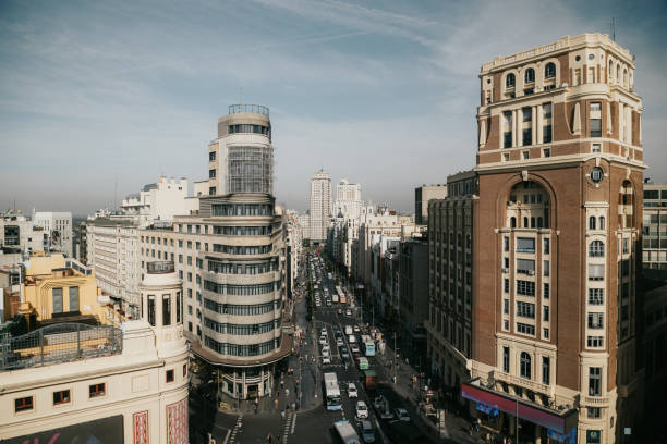An elevated view of Gran Vía, one of Madrid’s most iconic streets, bustling with life on a sunny morning. The architecture reflects a blend of the city’s classic charm and modern flair, with historical buildings standing alongside contemporary designs. The busy traffic below and the vibrant urban energy are captured from above, showing Madrid’s heartbeat in motion. Gran Vía is a perfect symbol of the city’s dynamic spirit and its seamless blend of history and modernity.