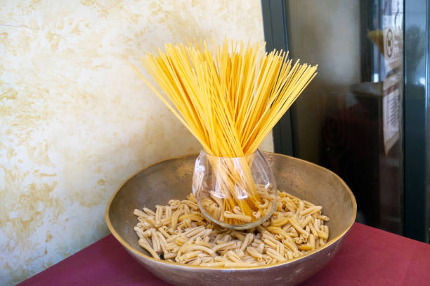 A creative arrangement of spaghetti and casarecce pasta placed in a glass vase and a brass bowl, providing a unique culinary display. ideal for a kitchen decor concept or food presentation inspiration.