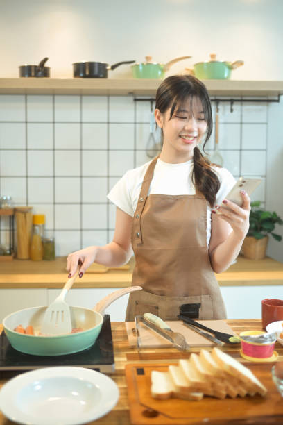 istock Smiling young woman using smartphone while preparing meal on a wooden worktop 2178831890