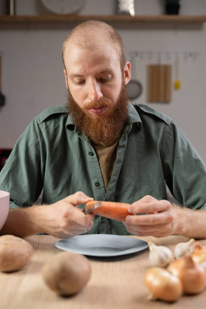 istock man peeling vegetable in kitchen sitting on the table with vegetables around 2178832118