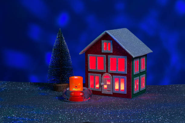 istock Halloween candle between red and green house with red light in windows and Christmas tree 2178834385